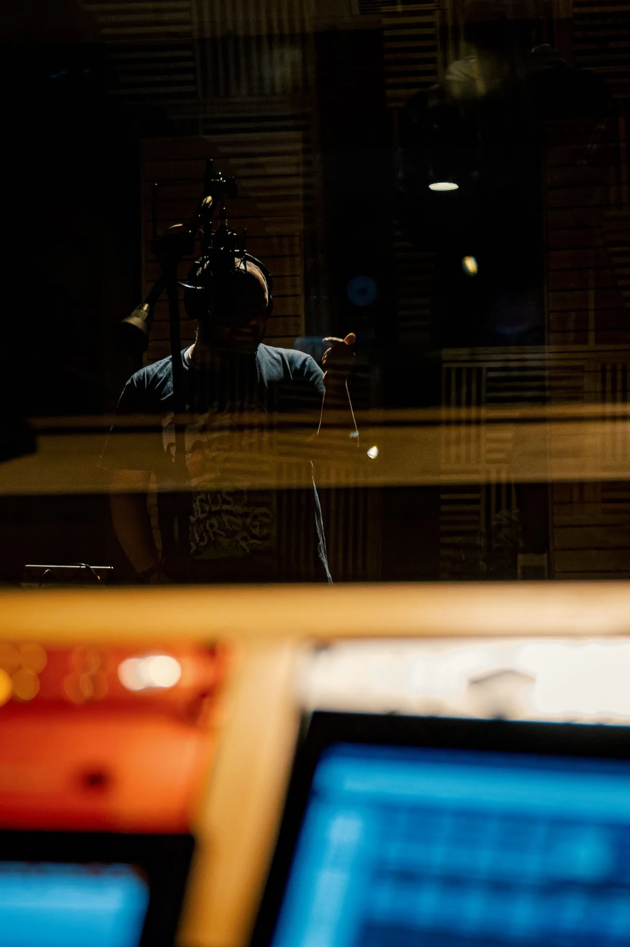 Vocalist tracking behind studio glass
